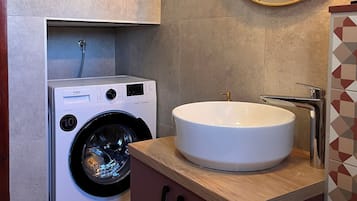 A modern bathroom with a built-in washing machine, a round mirror, and a sink with a chrome faucet.
