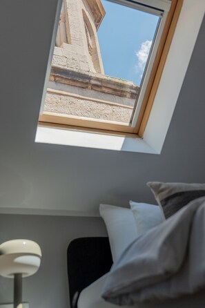 Une piĂšce avec une lucarne, un lit avec des oreillers et une lampe.