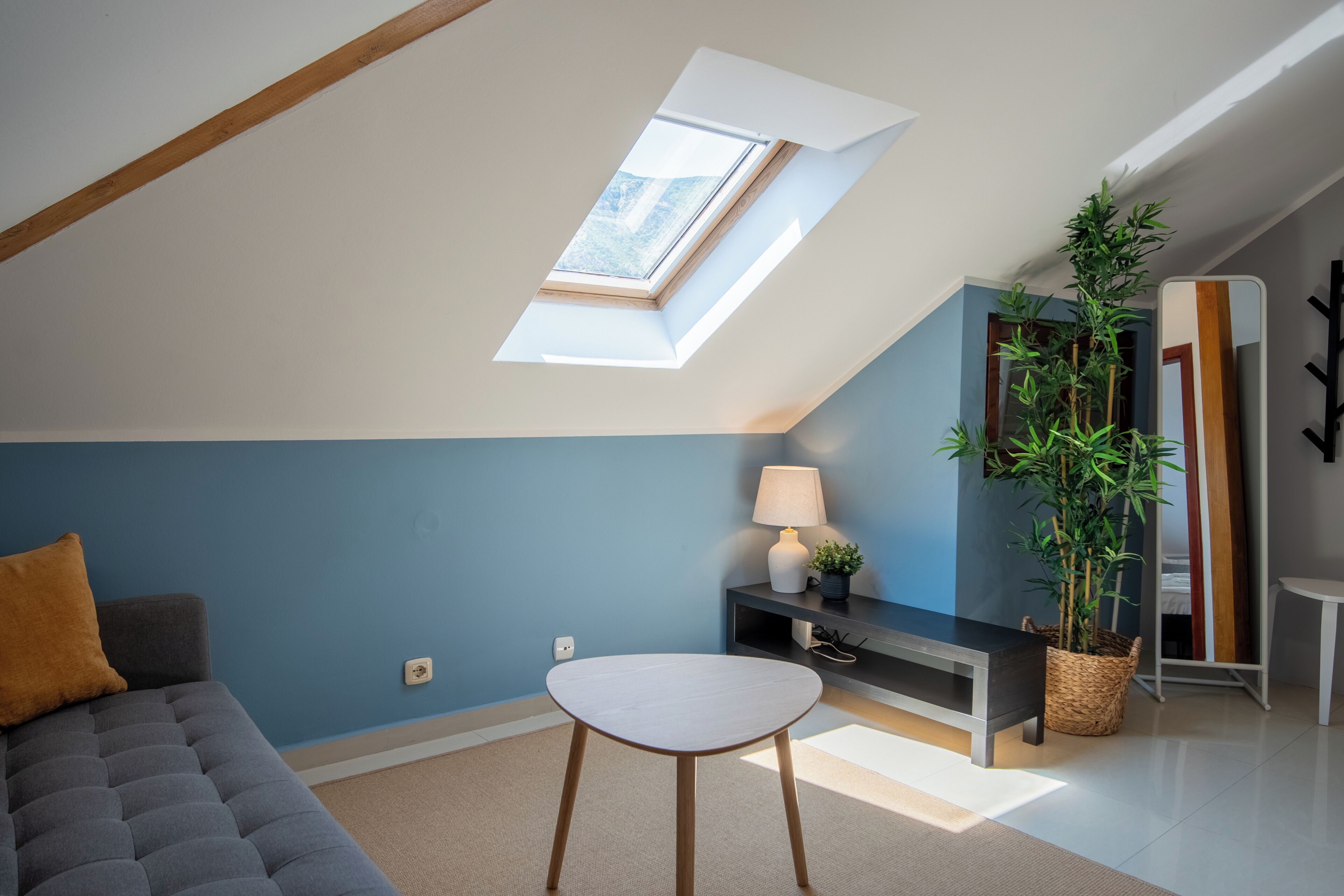 A modern living room with a skylight, a sofa, a table, a lamp, a plant, and a mirror.