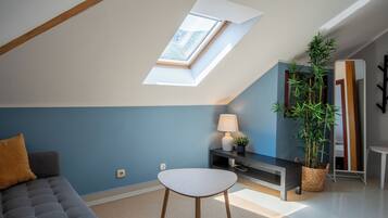 A modern living room with a skylight, a sofa, a table, a lamp, a plant, and a mirror.