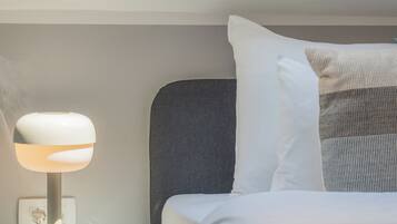 Un dormitorio con tragaluz, una mesita de noche con lámpara y una cama con almohadas.