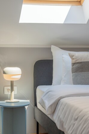 Une chambre avec un puits de lumiĂšre, une table de chevet avec une lampe et un lit avec des oreillers.