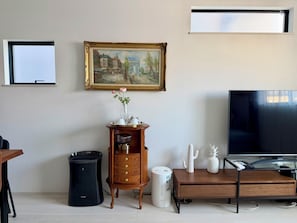A living room with a painting, a TV, a coffee maker, a cactus, and a pineapple.