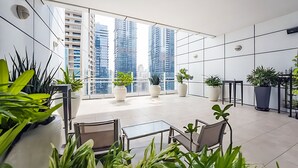 Ein moderner, gut beleuchteter Balkon mit großen Fenstern, Topfpflanzen und einem Glastisch.
