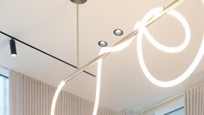 Ein modernes Interieur mit einem runden Tisch, einer schlichten Vase und einer außergewöhnlichen Deckenleuchte.