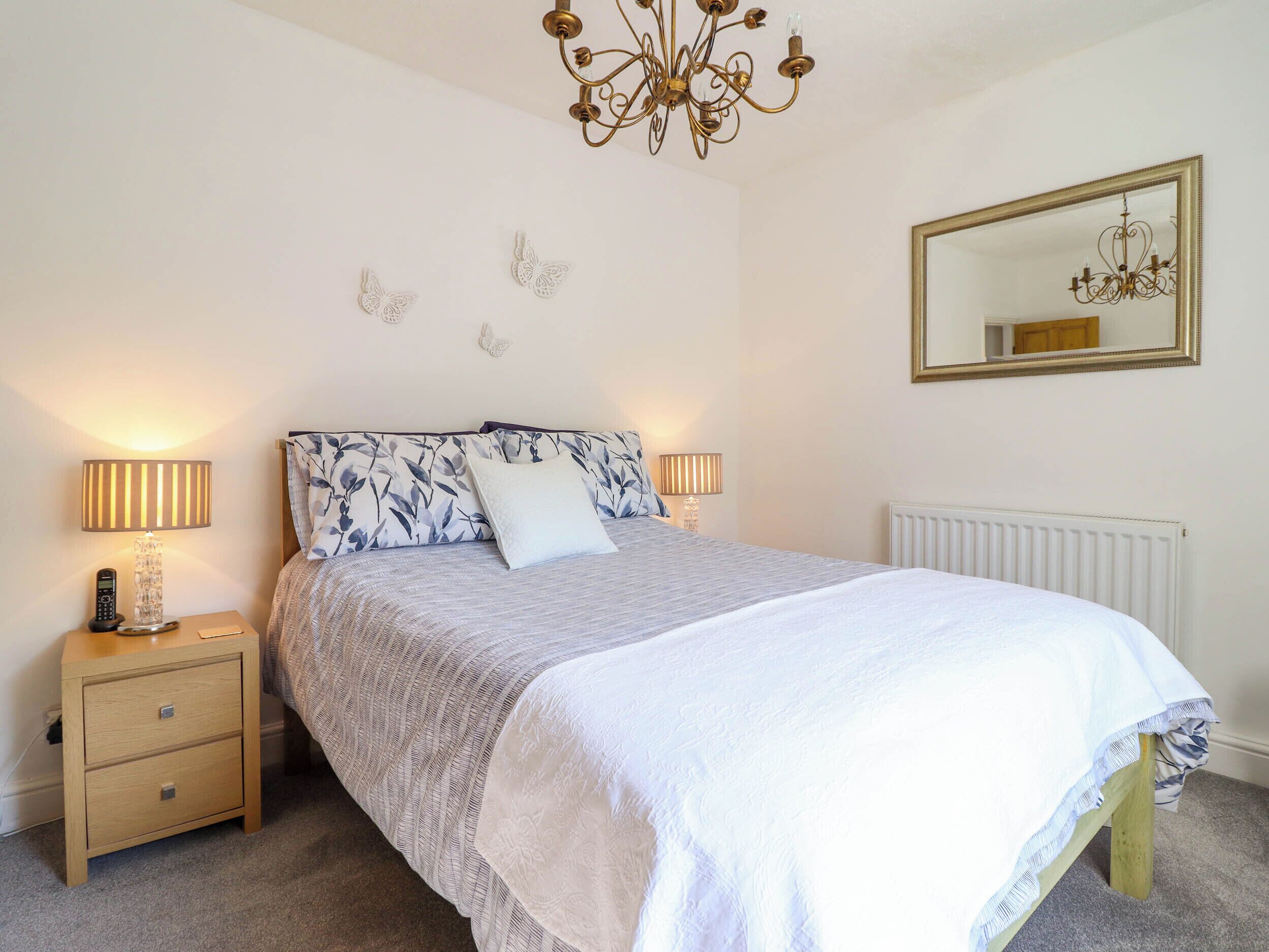 A bedroom with a bed, two bedside tables, a nightstand, a chandelier, a mirror, and wall decorations.