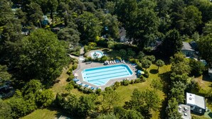 Vue aérienne d’un quartier résidentiel avec une piscine entourée d’arbres et de maisons.