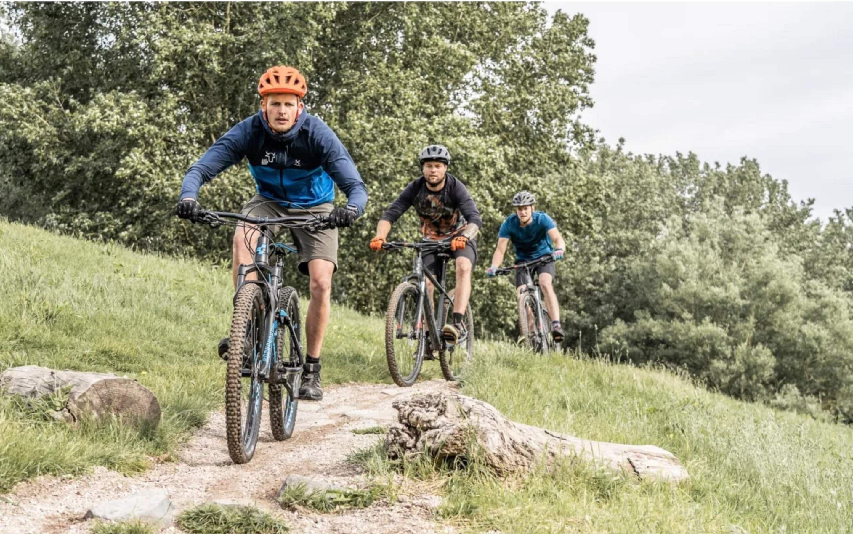 Drie mountainbikers op een onverhard pad, omringd door gras en bomen.