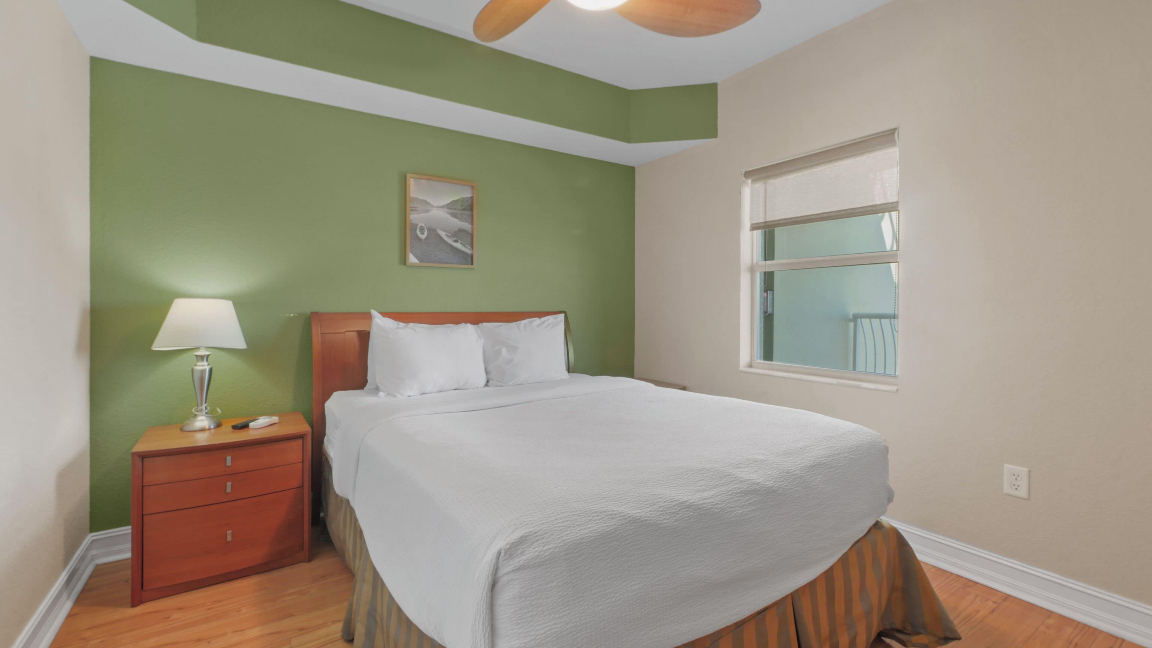 Quarto bem arrumado com cama, mesa de cabeceira, abajur e janela.