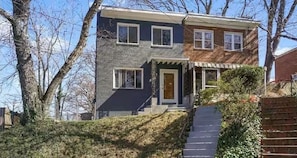 Une maison à deux étages avec un porche à l’avant, un escalier apparent et une façade en briques.