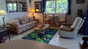 A living room with a sofa, chairs, a coffee table, a TV, and a window with curtains.
