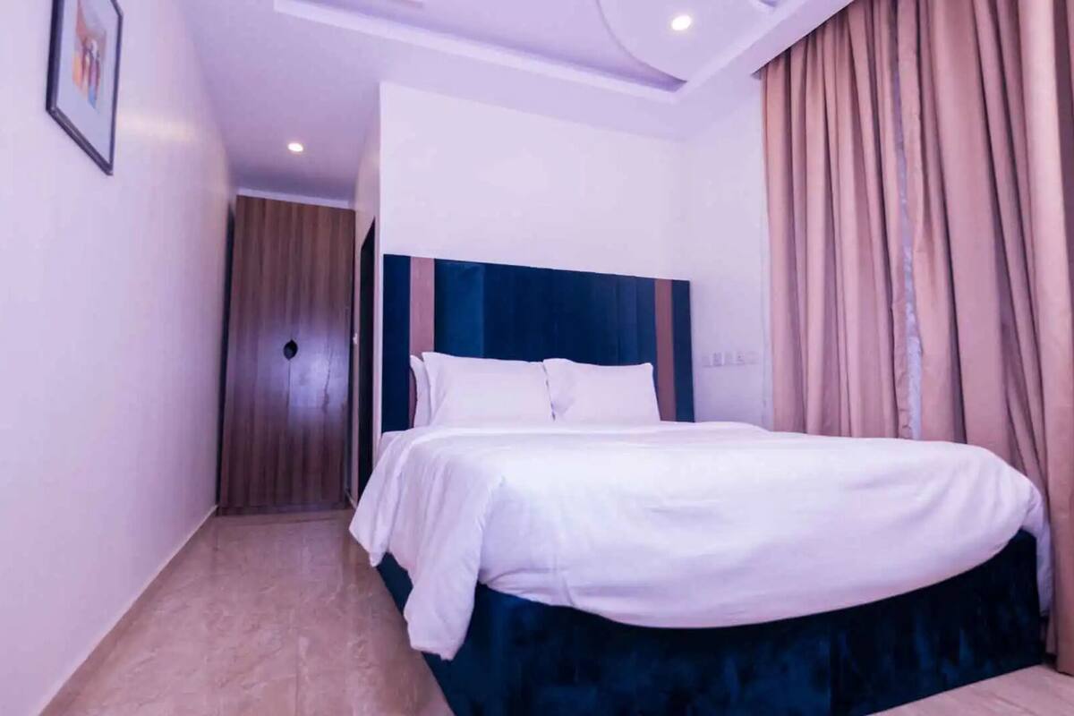Une chambre d’hôtel avec un lit, une tête de lit, une porte et un rideau.