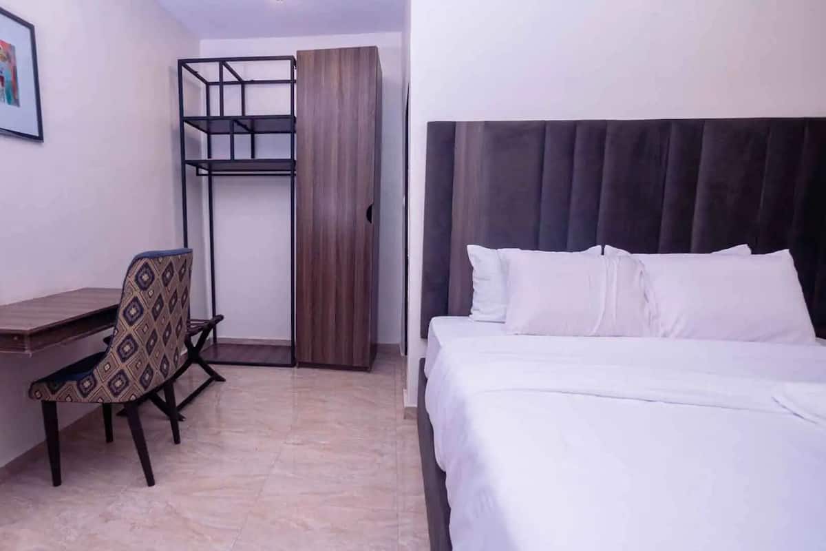 Une chambre d’hôtel avec un lit, un bureau, une chaise, une armoire et un tableau encadré au mur.