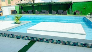 A swimming pool with tiled edges, a green wall, and outdoor seating. - Ibizza Pit Hotel and Suites (Lagos)
