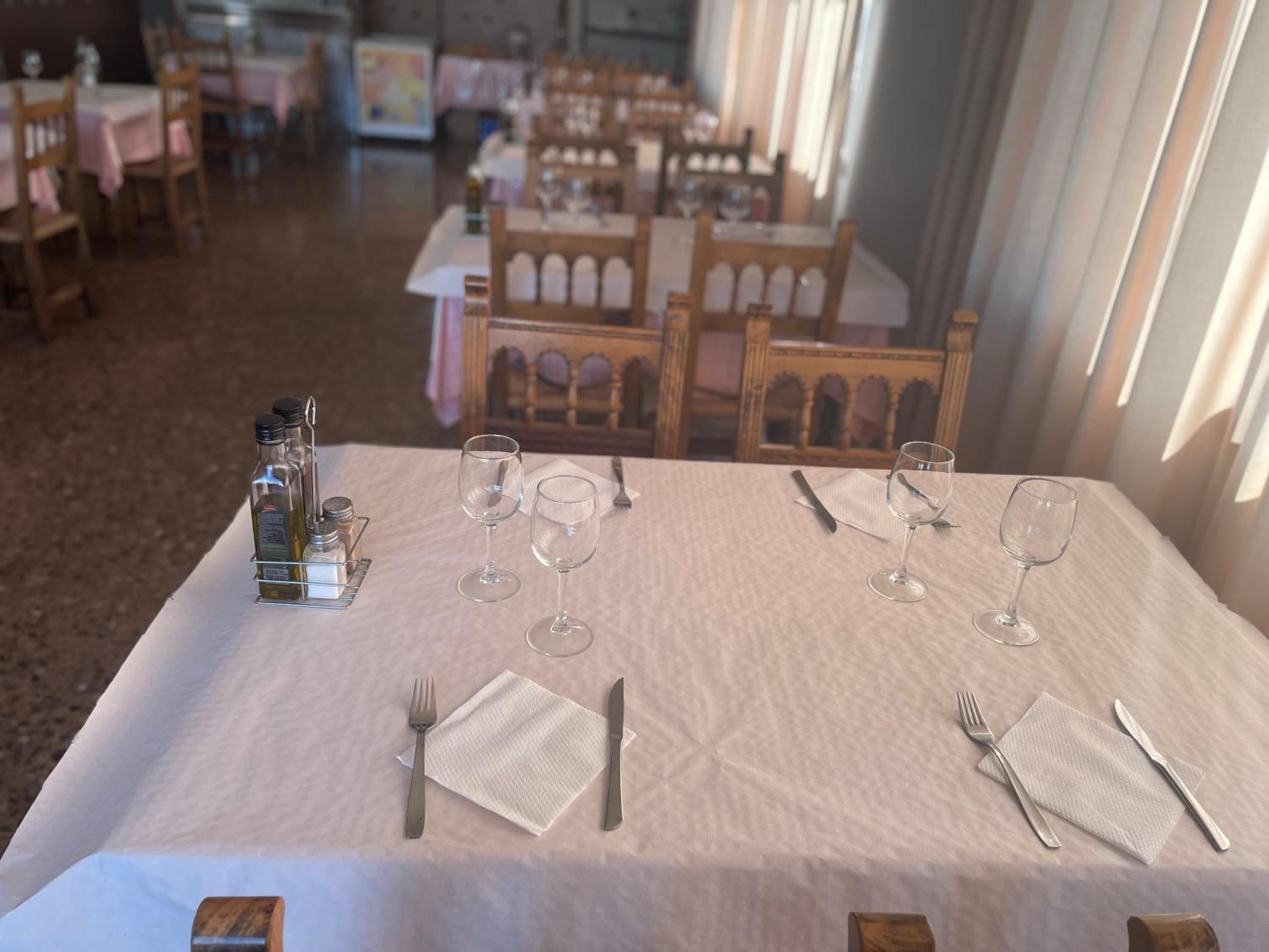 A dining area with tables set for four, each with wine glasses, cutlery, and condiments.