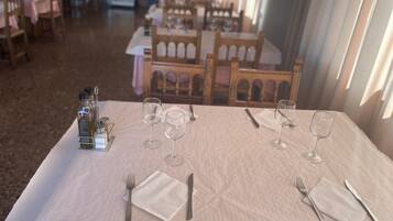 Comedor con mesas dispuestas para cuatro, cada una con copas de vino, cubiertos y condimentos.