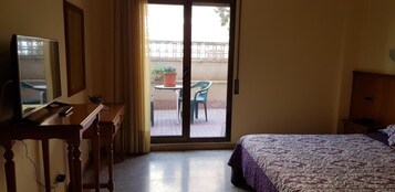 Habitación de hotel con una cama, un escritorio con computadora, una silla y un balcón con mesa y sillas.