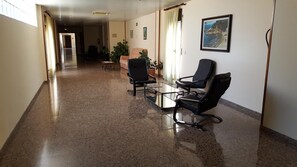 A hallway with a glass table and chairs, a potted plant, and a framed picture on the wall. - Hotel Reina Isabel (Lleida)