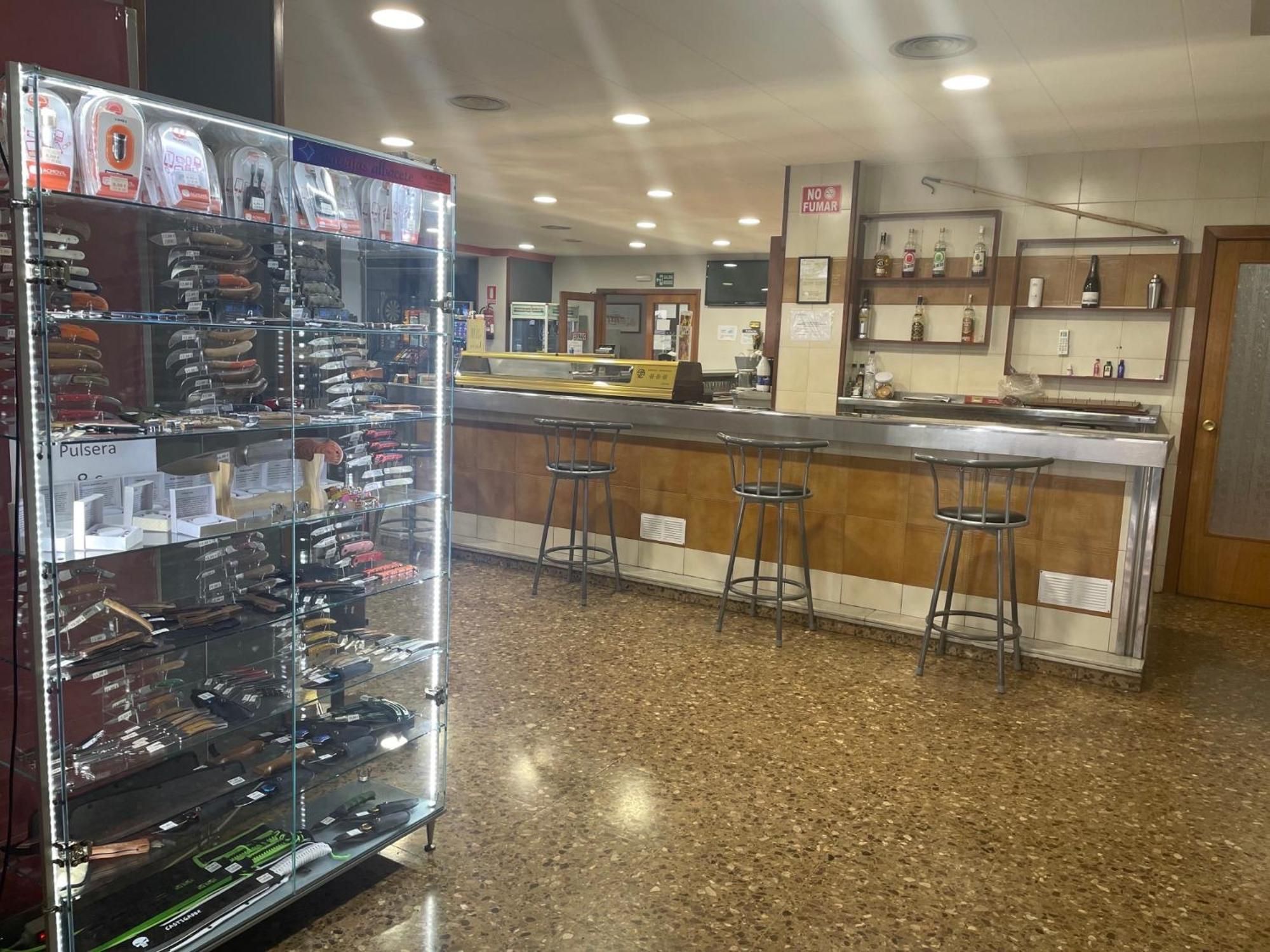 Una zona de bar con taburetes, mostrador y una vitrina con diversos artículos.