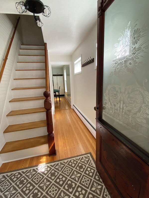 Un escalier avec des marches en bois et une rampe, menant à une pièce dotée d’un tapis à motifs et d’une porte ornée de vitraux.