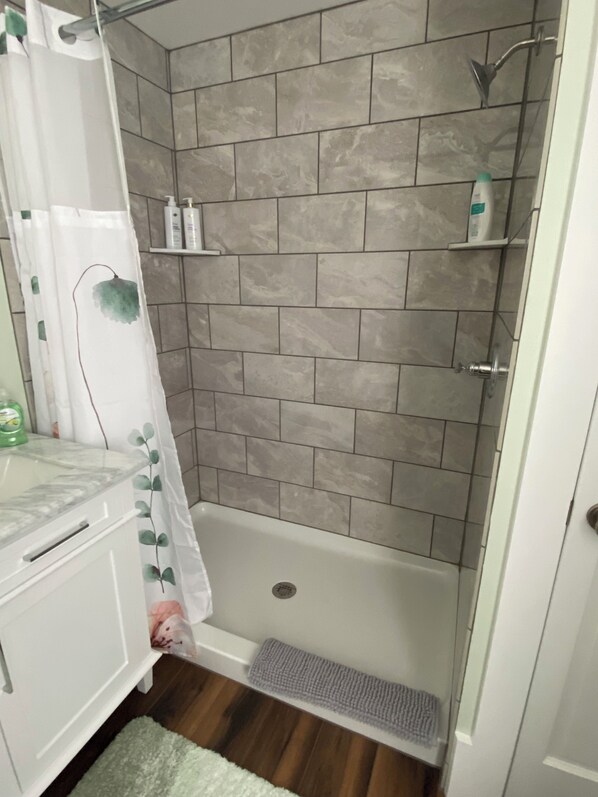 Une salle de bain avec une douche, des murs carrelés, un lavabo blanc et une plante verte.