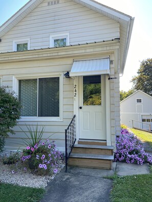 Une maison à deux étages avec une porte d’entrée blanche, un petit porche avec des marches et une boîte aux lettres.