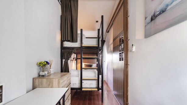 Un couloir étroit avec un lit superposé, une petite table sur laquelle est posé un vase de fleurs et un tableau accroché au mur.