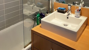 Un baño moderno con ducha envuelta en vidrio, un lavabo blanco sobre una cómoda de madera y un espejo grande sobre el lavabo.