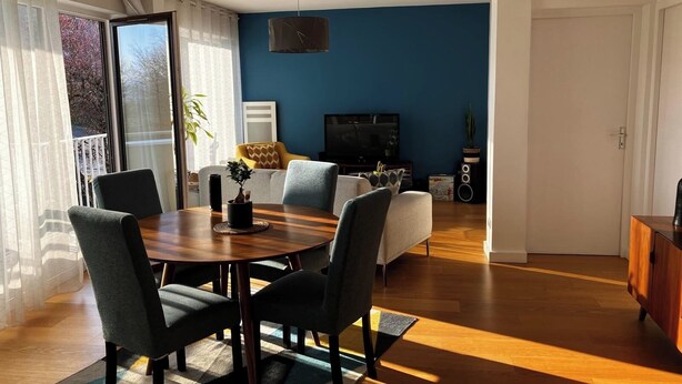 Una sala de estar moderna con una pared azul de acento, una zona de comedor con una mesa redonda y sillas, y un televisor al fondo.