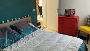 Un dormitorio con una cama, un aparador rojo, una silla amarilla y una puerta que da a un baño.