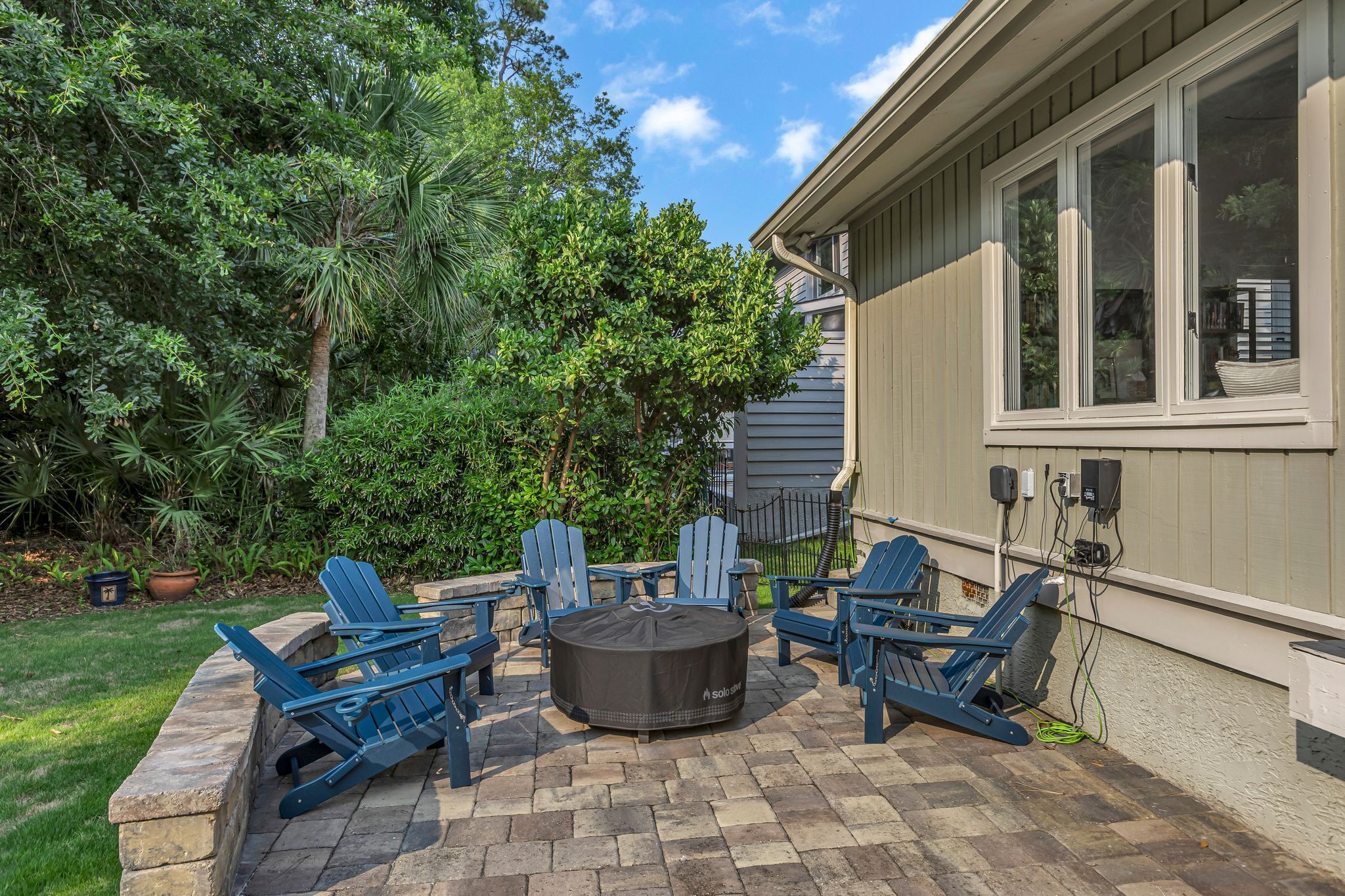 Une terrasse extérieure avec des fauteuils Adirondack et une table ronde, le tout entouré d’une végétation luxuriante.