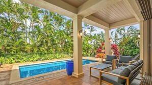 A covered outdoor area with a pool, lounge chairs, and a view of tropical vegetation.