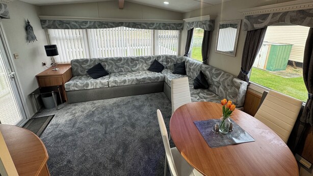 Interior de una caravana con sofá, mesa de comedor y una ventana pequeña.