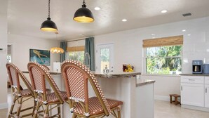 A kitchen with a central island, bar stools, pendant lighting, and a view of the outdoors. - 3 Blocks to Beach ☀️ Game room, cabana bar + family fun (Holmes Beach)