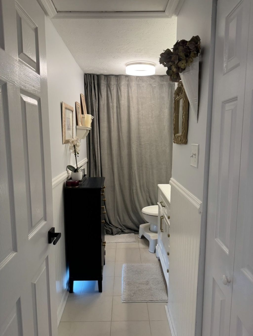 A narrow hallway leading to a bathroom with a toilet, sink, and a black cabinet.