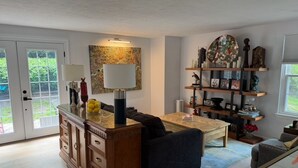 A living room with a coffee table, sofa, and a bookshelf with decorative items. - The Cozy Crab- Your Charming Haven in Lovely North Beach! (North Beach)
