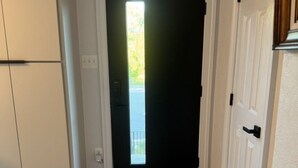 A hallway with a wooden floor, a white door with a black frame, and a small window at the end. - The Cozy Crab- Your Charming Haven in Lovely North Beach! (North Beach)