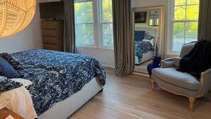 A bedroom with a bed, a chair, a dresser, and a window with curtains. - The Cozy Crab- Your Charming Haven in Lovely North Beach! (North Beach)