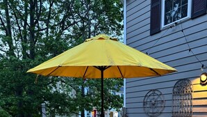 An outdoor patio with a round table and chairs, a yellow umbrella, and a wooden deck. - The Cozy Crab- Your Charming Haven in Lovely North Beach! (North Beach)