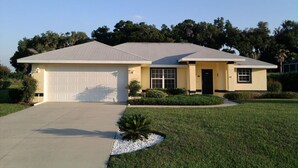 A single-story house with a garage, a front yard with a small garden, and a clear sky. - Inverness Florida 4BR Pool Home & Spa – Near Ocala, Crystal River & Floral City (Inverness)