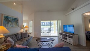 A living room with a sofa, a coffee table, a TV on a wooden stand, and a painting on the wall. - Inverness Florida 4BR Pool Home & Spa – Near Ocala, Crystal River & Floral City (Inverness)