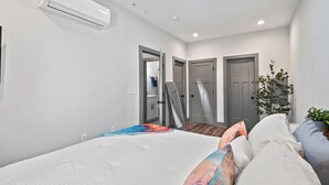 A modern bedroom with a bed, air conditioning unit, and a door leading to another room.