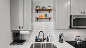 A modern kitchen with a stainless steel sink, a coffee maker, a kettle, and a microwave.