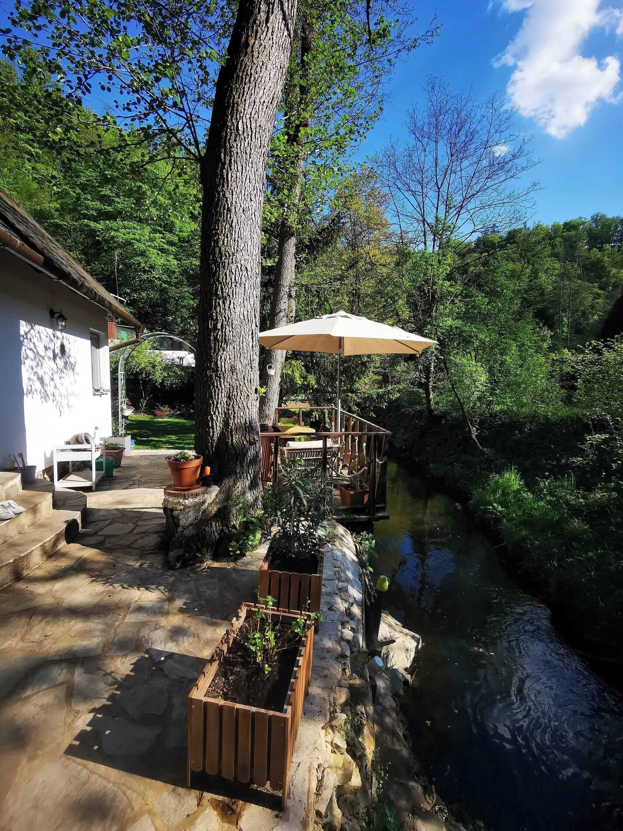 Un patio de piedra con mobiliario exterior, una jardinera de madera y una pérgola con sombrilla.