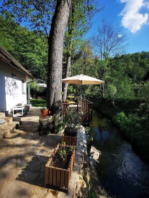 A stone patio with outdoor furniture, a wooden planter, and a pergola with an umbrella. - Fairy Tale Cottage on Water Stream, 30 Minutes From South Prague (Petrov)