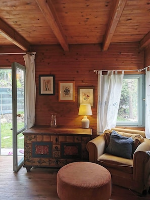 Interior acogedor de una caba ña con paredes de madera, un banco acolchado, una mesita con una lámpara y cuadros en la pared.
