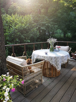 Une terrasse en bois, meublée de meubles en osier et agrémentée d’une table recouverte d’une nappe à motifs.