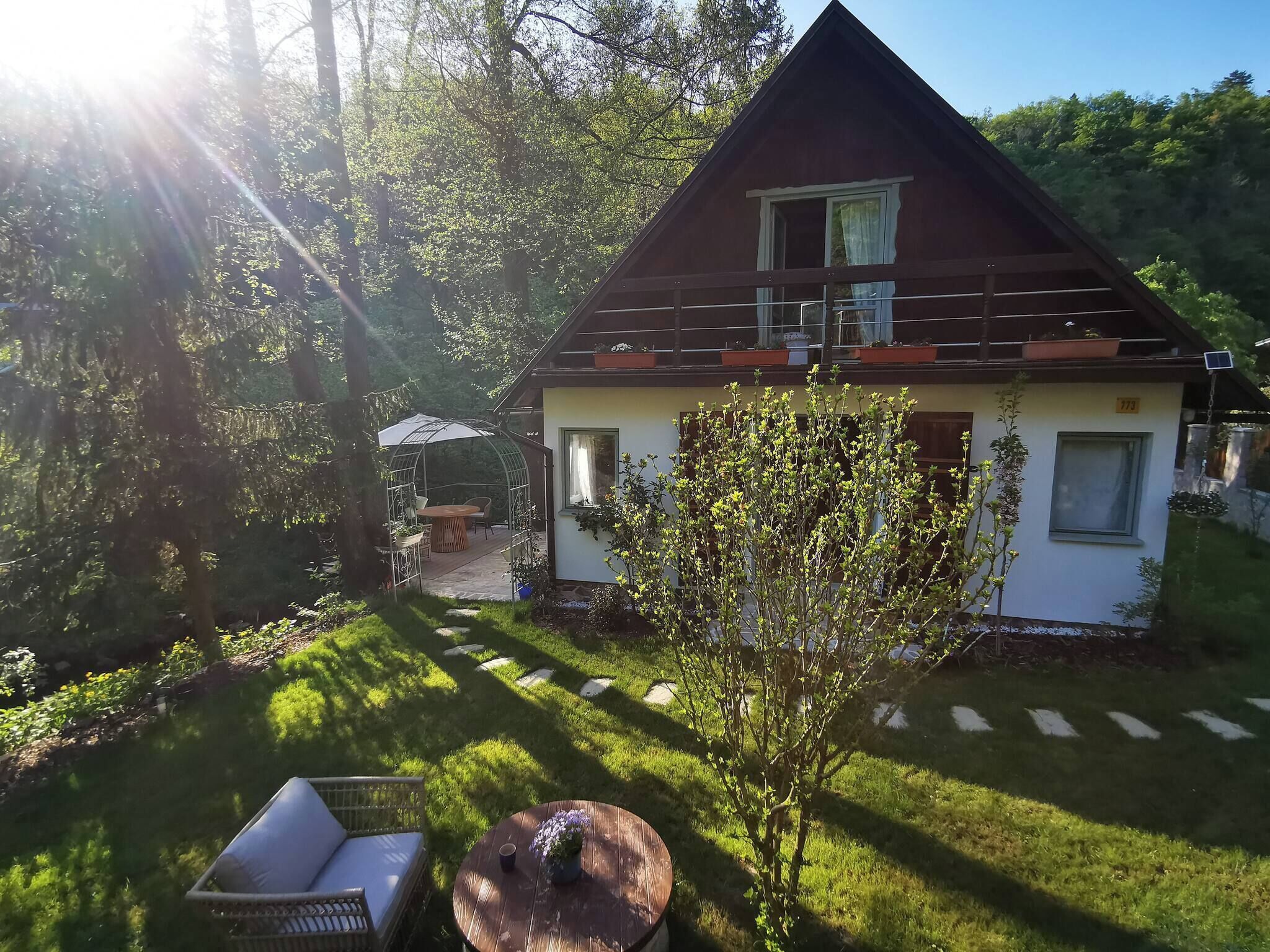 A house with a garden, a patio with a table and chairs, and a small tree.