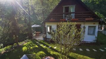 A house with a garden, a patio with a table and chairs, and a small tree.