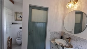 Egy fürdőszoba, zöld ajtóval, WC-vel, márvány mosdókagylós mosdóval és a falra szerelt tükörrel.